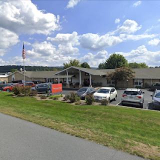 A view of a building with a parking lot, surrounded by grassy areas and under a cloudy sky.