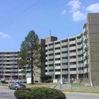 A large, multi-story apartment building under a clear blue sky with parked cars in the foreground.