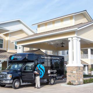A shuttle bus parked at the entrance of a building, with a person standing nearby.