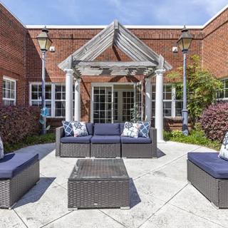 A cozy outdoor seating area with wicker furniture in a courtyard bordered by a brick building.
