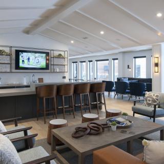 A modern living room with an open bar area and comfortable seating, featuring a television and stylish wooden furniture.