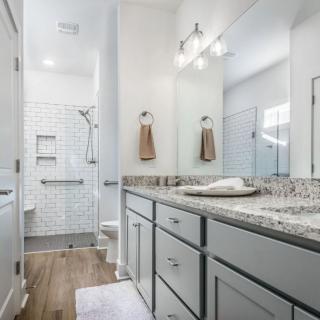A modern bathroom with a large mirror, granite countertop, and a walk-in shower.