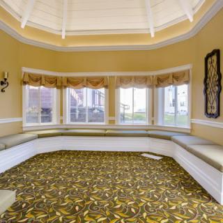 An empty room with a patterned carpet and built-in seating beneath large windows.
