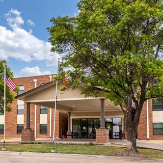 A hotel entrance with flags and a large tree under a partly cloudy sky.