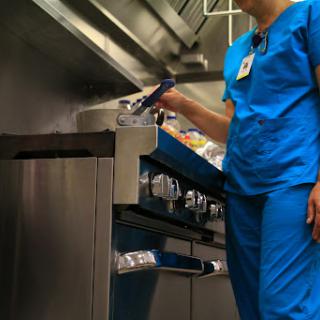 A healthcare worker in blue scrubs prepares food in a kitchen setting.