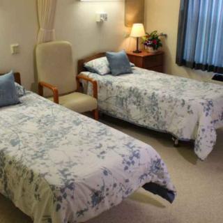 A cozy bedroom with two single beds, each adorned with floral-patterned bedding. A wooden nightstand with a lamp sits between them, alongside a comfortable chair.