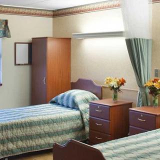 A shared hospital room with two beds, a wardrobe, and bedside tables decorated with flowers.