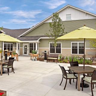 A sunny patio with tables, chairs, and umbrellas outside a building.