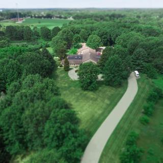 Aerial view of a house surrounded by lush greenery and a winding driveway.