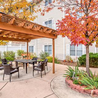 A cozy patio with a pergola and outdoor seating, surrounded by autumn foliage.