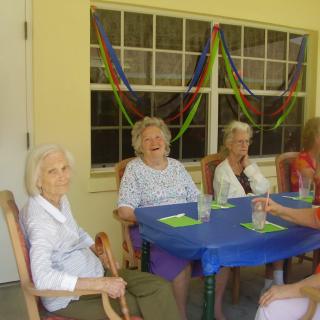 A group of elderly women sitting around a table with festive decorations in the background.
