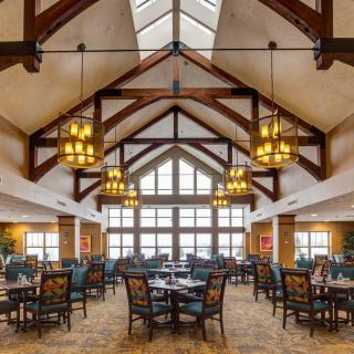 A spacious dining area with high ceilings and chandeliers, featuring wooden beams and large windows.
