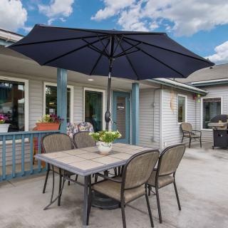 A cozy outdoor patio setup with a table, chairs, and a large umbrella under a partly cloudy sky.