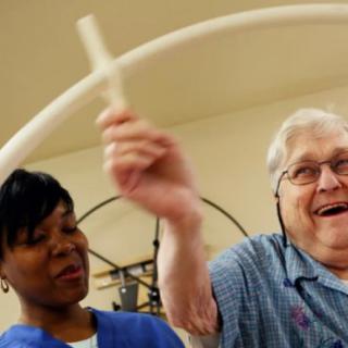 A healthcare worker assists an elderly person during a physical therapy session.