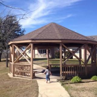 A child walking towards a wooden gazebo on a sunny day.