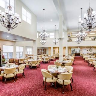 A spacious dining area with elegant chandeliers and neatly arranged tables and chairs on a red carpet.