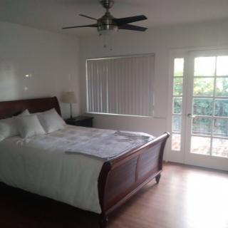 A cozy bedroom with a wooden bed, ceiling fan, and French doors leading outside.