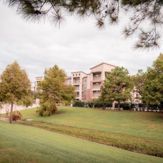 A scenic view of apartment buildings surrounded by lush greenery and trees under a cloudy sky.
