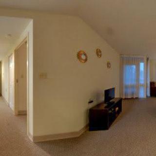 A spacious living room with a television, decorative plates on the wall, and an adjoining hallway.