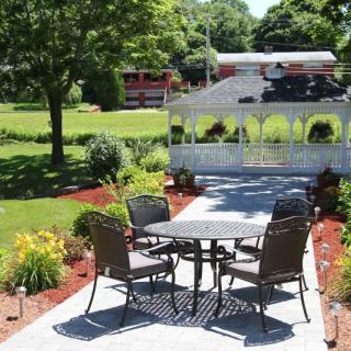 A sunny garden with a patio set and gazebo surrounded by lush greenery.
