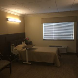A quiet hospital room featuring a single bed, a chair, and a window with blinds.