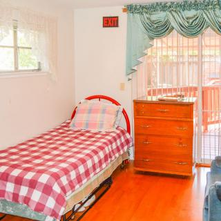A cozy bedroom with a single bed and plaid bedding, featuring a window, chest of drawers, and hardwood flooring.