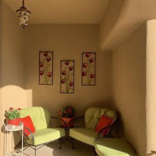 A cozy outdoor seating area with green chairs, colorful cushions, and decorative wall art.