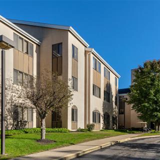 A modern residential building surrounded by greenery and a clear blue sky.