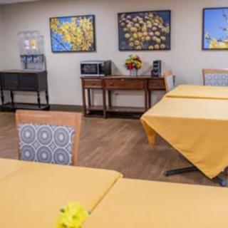 A dining room with yellow tablecloths and floral wall art.