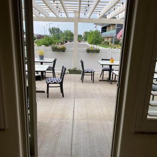 A view from inside looking out to a modern patio with tables and chairs under a spacious canopy.