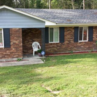A suburban brick house with a well-maintained lawn and a plastic chair on the porch.
