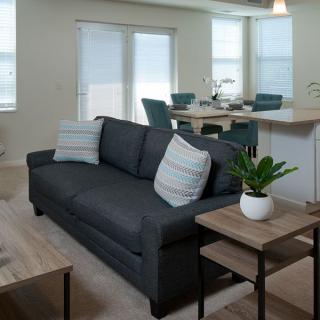 A modern living room with a dark sofa, accent pillows, and nearby dining area.