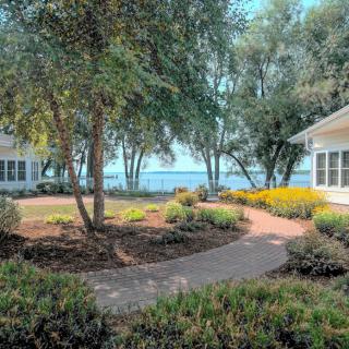 A serene garden pathway winds between lush greenery, leading to a scenic view of a lake beyond.