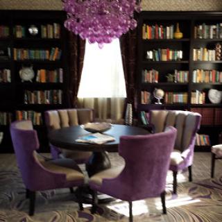A stylish dining area featuring purple chairs and a modern chandelier, surrounded by bookshelves filled with books.