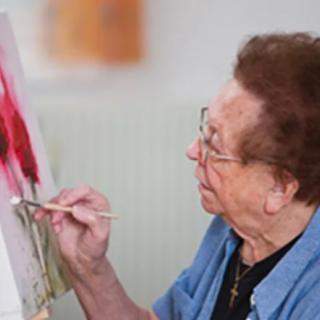 An elderly woman engaged in painting at her easel.