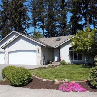A suburban house with a well-maintained garden and driveway, surrounded by tall trees.