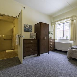A cozy bedroom interior with a wardrobe, chest of drawers, and a window.