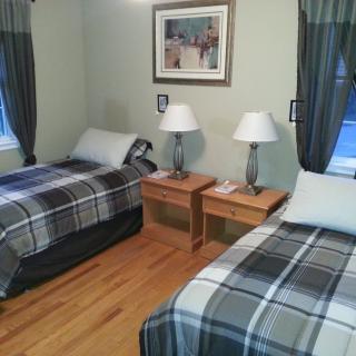 A neatly arranged bedroom with twin beds featuring plaid bedding, two lamps on wooden nightstands, and elegant curtains.