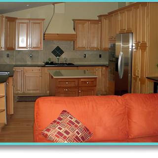An open concept kitchen and living room area featuring wood cabinets and a stainless steel refrigerator, with an orange sofa in the foreground.