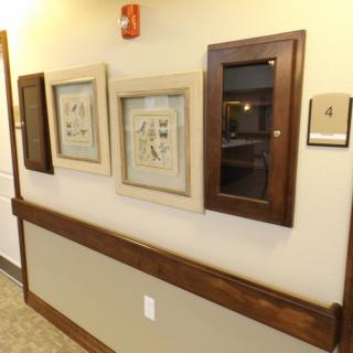 A hallway with framed artwork and a display case mounted on the wall.
