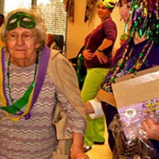 An elderly woman wearing a festive mask and beads at a celebration.