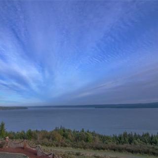 A tranquil landscape view of a lake under a vast blue sky with scattered clouds.