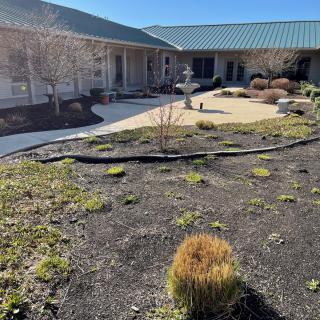 A courtyard with a garden, paved path, and fountain in front of a building.
