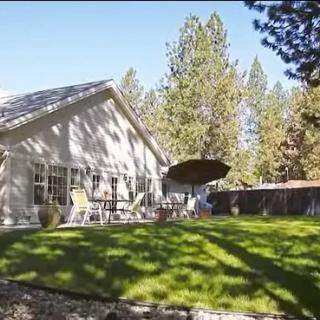 A serene backyard with a well-maintained lawn, patio furniture, and tall trees under a clear blue sky.