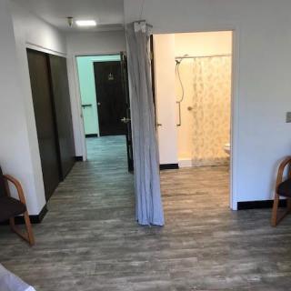A spacious room with wooden flooring, two chairs, a curtain dividing the area, and a view into a bathroom with a shower.