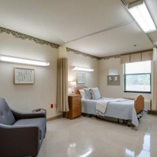 A clean and organized hospital room with a bed and seating area.