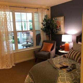 A cozy bedroom with warm lighting, featuring an armchair by a large window and stylish decor.