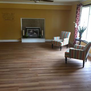 A cozy living room featuring comfortable chairs, a fireplace, and warm yellow walls, illuminated by natural light.