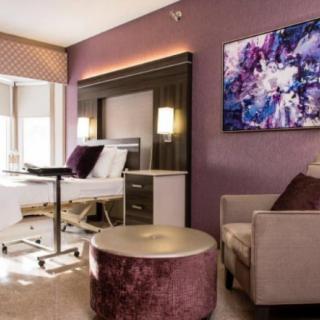A modern hospital room with elegant interior design, featuring a comfortable chair, a hospital bed, and abstract artwork on the wall.
