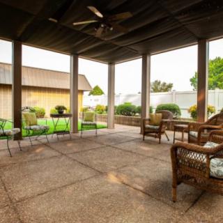 A cozy covered patio with wicker furniture overlooking a garden.